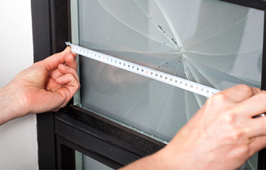 Mit einem Zollstock wird an einem kaputten Fenster Maß genommen